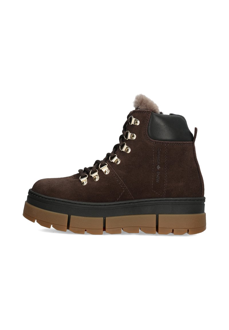 Braune Wildleder-Ankle-Boots mit schwarzen Lederakzenten, goldenen Metallösen und einer dicken, strukturierten Gummisohle. Flauschiges Futter an der Oberseite.