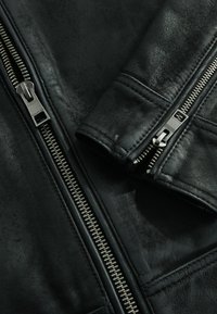 Zwarte leren jas met zilveren ritsen, een gladde textuur en gedetailleerde stiksels aan de manchetten en kraag.