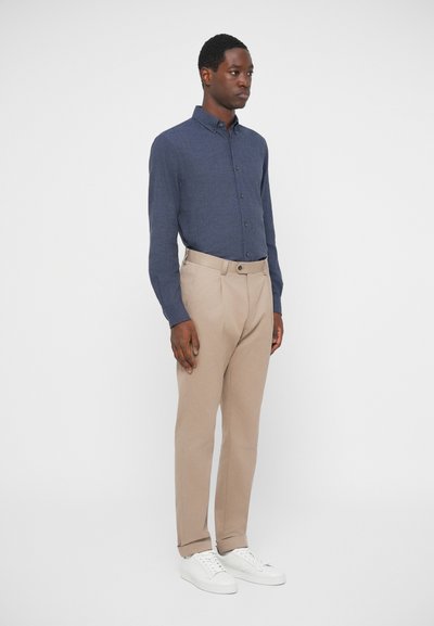 Garais piedurkņu zils pogāts krekls apvienots ar bēšām biksēm un baltajiem tenisiem. Krekls ir ar austiem rakstiem un klasisku apkakles dizainu.