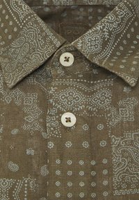 Bruine overhemd met een bandana-ontwerp en witte accenten, korte kraag en twee crèmekleurige knopen.