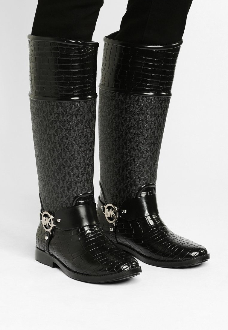 Bottes montantes imperméables noires en caoutchouc, présentant un dessus en faux crocodile texturé, un tige en tissu avec un motif de logo, et un détail de boucle métallique.