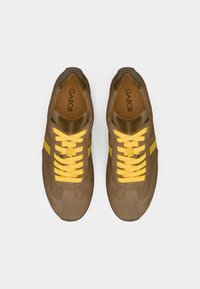 Καφέ σουέντ αθλητικά παπούτσια με κίτρινες κορδόνια και πλαϊνές ρίγες. Διαθέτουν στρογγυλεμένη μύτη και επένδυση στο πέλμα. Η εσωτερική σόλα φέρει τη σήμανση "GABOR".