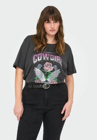Yli suuri hiiliharmaa t-paita, jossa on graafinen kuvasto, jossa on siipiä, ruusuja ja "COWGIRL"-teksti vaaleanpunaisena. Yhdistetty korkeavyötäröisten mustien housujen kanssa.