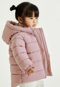 Doudoune rose clair avec capuche, poignets côtelés, couture diagonale et fermeture éclair intégrale. Texture douce adaptée aux temps froids.