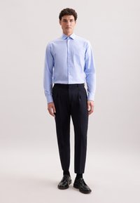 Lichtblauw langslijf shirt met een button-down kraag en een borstzak, gecombineerd met donkere broek en zwarte veterschoenen.