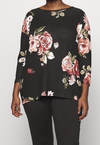 Black top with floral print in shades of pink and green. Features three-quarter sleeves and a loose, curved hem design. Soft fabric texture.