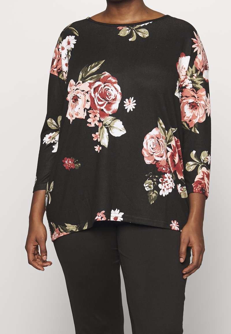Black top with floral print in shades of pink and green. Features three-quarter sleeves and a loose, curved hem design. Soft fabric texture.