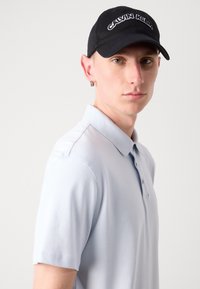 Šviesiai mėlynas polo marškinėliai su klasikiniu apykakle ir trimis mygtukais. Juoda kepurė su „CALVIN KLEIN“ logotipu. Lygus audinio paviršius.