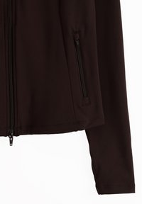 Manga y lateral de chaqueta negra que muestra un bolsillo vertical con cremallera y cremallera frontal parcialmente cerrada sobre fondo blanco.