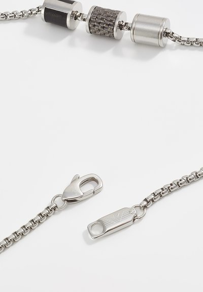 Metalen ketting met cilindrische schakels in zilver, met getextureerde accenten en zwarte details. Inclusief een lobsterclasp en een gegraveerd label.
