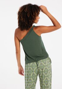 Top sin mangas verde de un solo hombro con un ajuste holgado y textura suave, combinado con pantalones verdes y amarillos estampados que presentan diseños intrincados.