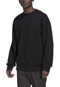 Juodas džemperis, pagamintas iš medvilnės ir sintetinių pluoštų mišinio, su apvalia iškirpte, ilgomis rankovėmis, raišteliais ir diskretišku logotipu ant krūtinės.