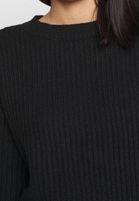 Schwarzer Rippstrickpullover mit Rundhalsausschnitt und strukturiertem Stoff, der ausgeprägte vertikale Streifen und eine weiche Oberfläche zeigt.