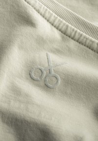 Tessuto grigio chiaro con una texture liscia; presenta un design di forbici ricamato in un grigio leggermente più scuro. Vista ravvicinata del materiale.