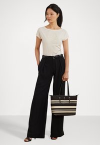 Beige cotton t-shirt with floral print, high-waisted black trousers, and a patterned black and cream striped tote bag. Black open-toe shoes.