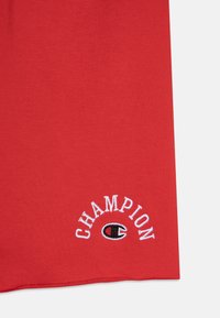 Rotes Baumwoll-T-Shirt mit gesticktem "Champion"-Logo und kreisförmigem Akzent. Glatte Textur, kurze Ärmel und Rundhalsausschnitt.