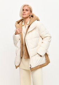 Puffjakke med et cremefarvet ydre lag og et brunt indre lag, udstyret med en stor hætte, trykknaplukning og quiltet design til isolering.