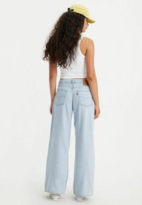 Jeans a gamba larga di colore blu chiaro realizzati in denim, con vita alta, orlo arrotolato e tasche posteriori dotate di un'etichetta in pelle marrone con il marchio.