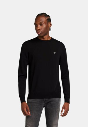 Maglione lungo nero con maniche a manica lunga, colletto a girocollo, polsini a coste e un piccolo logo triangolare sul lato sinistro del petto. Il tessuto appare liscio.