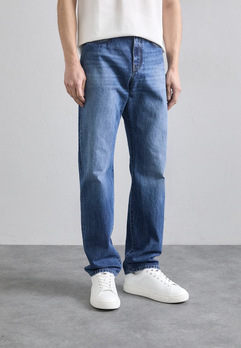 Jeans din denim de un albastru deschis, cu croi drept, având cusături vizibile și un design cu cinci buzunare, asortați cu adidași albi.