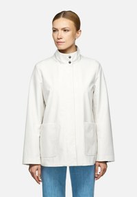 Giacca impermeabile bianca con colletto alto, chiusura frontale con bottoni a pressione e due grandi tasche. Tessuto liscio con design minimalista.