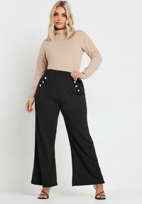 Vida högmidjade svarta byxor med vida ben, prydda med glansiga knappdetaljer på framfickorna, i kombination med en långärmad beige topp.