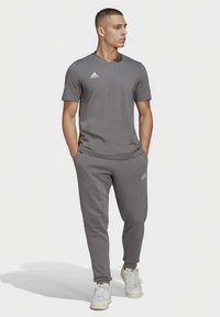 Szürke sportos szett, rövid ujjú pólóval és szűkített szárú nadrággal. Simogató anyagból készült, az Adidast logóval a mellkason és a lábszáron.