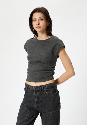 Top corto gris acanalado con mangas cortas y lados fruncidos, combinado con pantalones cargo negros de cintura alta. Textura suave, diseño ajustado.