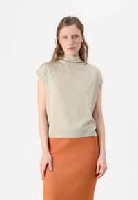 Lys beige, kortermet topp med høy hals, parret med et teksturert oransje ribbestrikket skjørt. Antrekket har en tettsittende silhuett.