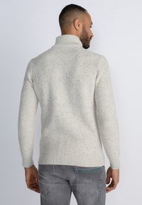 Pulover tricotat texturat de culoare gri deschis, cu un guler înalt și manșete striate. Prezintă un model cu puncte și o siluetă ajustată.