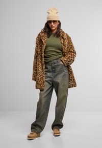 Løveprikket faux fur-kåpe, olivengrønn genser, løse grå jeans og beige lue. Briller og beige slip-on sko fullfører stilen.