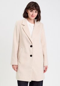 Manteau en mélange de laine beige à devant simple boutonné, deux boutons noirs, revers crantés et poches latérales. Coupe droite et manches longues.