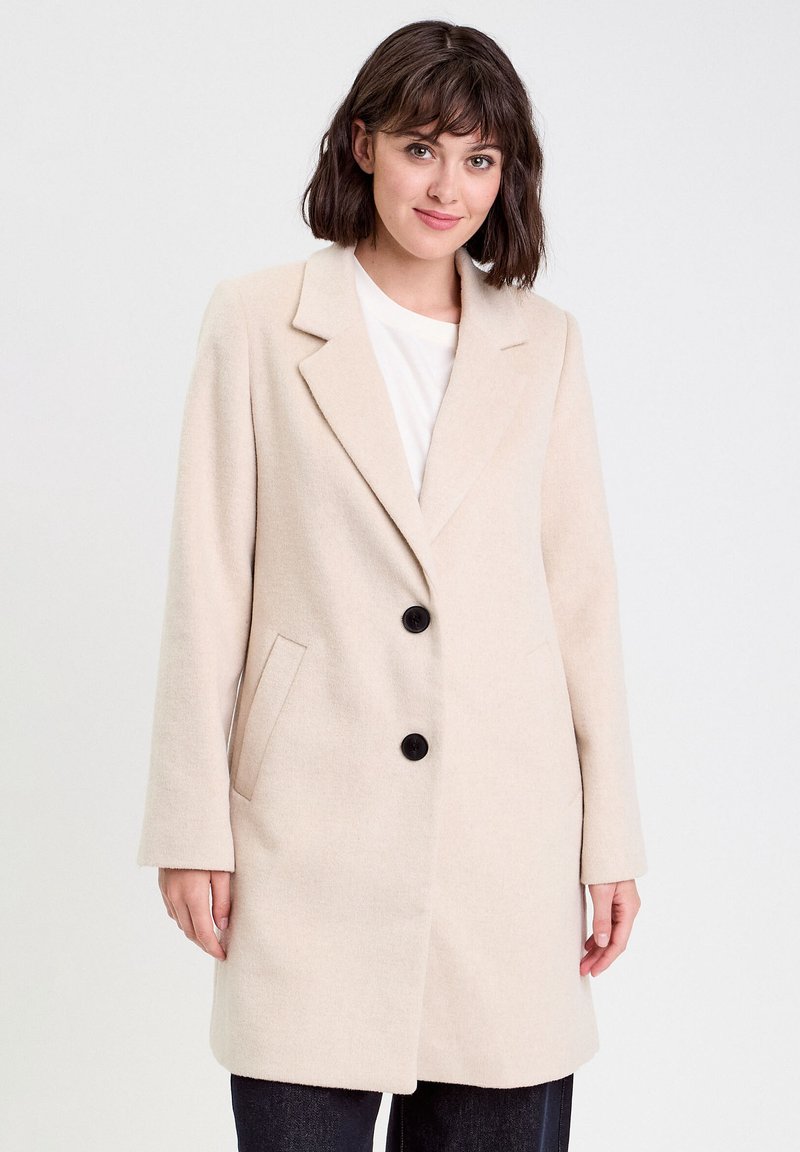 Manteau en mélange de laine beige à devant simple boutonné, deux boutons noirs, revers crantés et poches latérales. Coupe droite et manches longues.