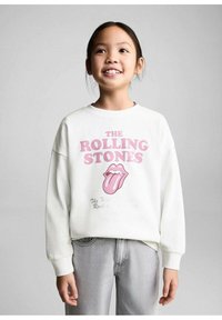 Felpa bianca con il testo e il logo dei "The Rolling Stones" in rosa. Tessuto morbido con una vestibilità comoda e polsini a coste. Indossata con jeans grigi.