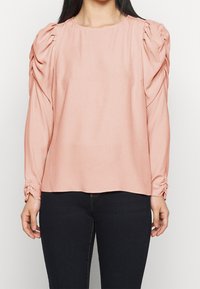 Světle růžová halenka s dlouhými rukávy, s nařasenými balónovými rukávy a staženým detail pod zápěstím, vyrobená z měkké tkaniny, s kulatým výstřihem.