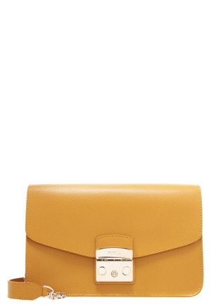 Musztardowożółta skórzana torba na ramię z srebrnym zamkiem zatrzaskowym i regulowanym paskiem, leżąca płasko na białym tle.