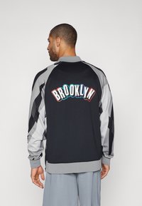 Black and gray jacket with a ribbed collar. "BROOKLYN" graphic in multicolor on the back. Features contrasting sleeves and a smooth texture.