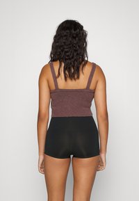 Brun strikket crop top med tykke stropper, kombinert med høytlivede svarte shorts. Teksturen er myk og ribbet.