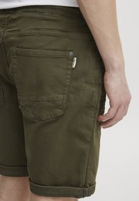 Șorturi din bumbac verde măsliniu, cu manșete rulabile, două buzunare la spate și un eticheta mică lângă talie. Textură netedă și design casual.