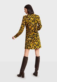 Keltainen pitkähiha dressi, jossa on musta- ja oranssikirjava leopardikuvio, ja taakse sidottava yksityiskohta. Yhdistetty polven korkeisiin ruskeisiin nahkasaappaisiin.