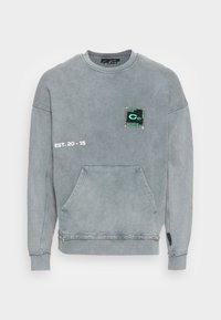 Szary sweter typu pulower z przednią kieszenią, postrzępionym dołem i naszywką na klatce piersiowej z wielokolorowym wzorem oraz napisem "EST. 20 - 15."