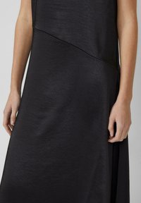 Zwarte jurk met een zachte, gestructureerde stof, een asymmetrisch ontwerp en naaddetails. Close-up van een hand op de stof.