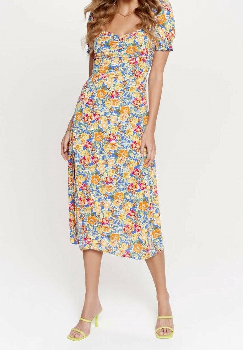 Robe midi florale ornée de fleurs jaunes, oranges et rouges vives sur un fond bleu, avec des manches courtes bouffantes et un corsage ajusté.