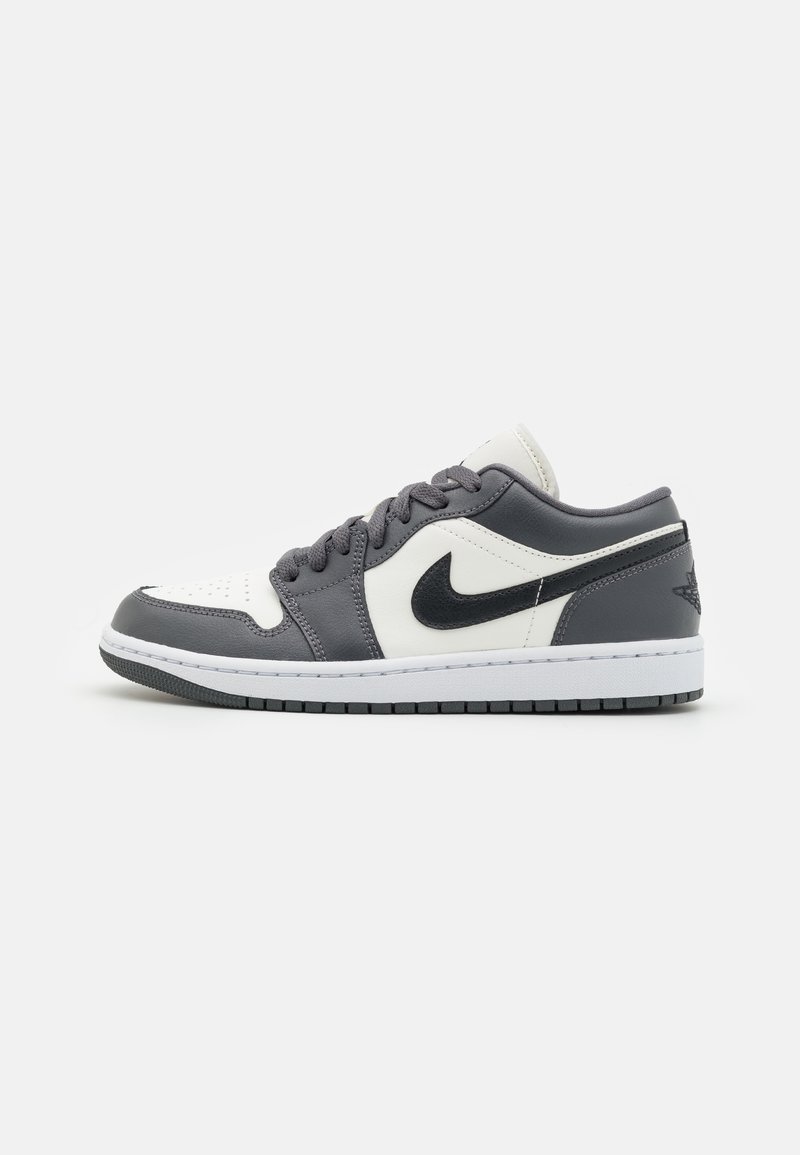 Basket basse Nike blanche et grise avec logo swoosh noir, bout perforé, lacets plats gris et semelle blanche avec semelle extérieure noire.