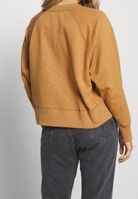 Senapsgul sweatshirt med en avslappnad passform, raglanärmar, ribbade muddarna och en strukturerad tyg. Kombinerad med mörkgrå denim.