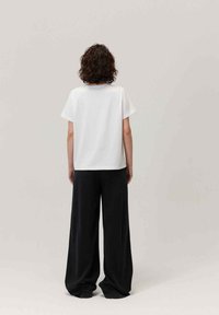 Biała bawełniana koszulka z krótkim rękawem, prosty krój, widok z tyłu, zestawiona z luźnymi czarnymi spodniami. Minimalistyczny design.