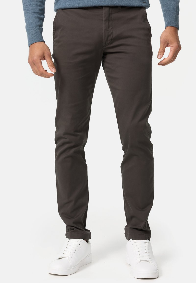 Donkerbruine, slim-fit chinos van soepel materiaal. Voorzien van een standaard tailleband en zakken, gecombineerd met witte sneakers voor contrast.