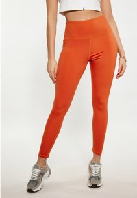 Těsně padnoucí oranžové legíny s vysokým pasem, vyrobené z elastického materiálu. Design obsahuje ploché švy a hladkou strukturu.