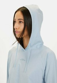 Lichtblauwe hoodie met een zachte textuur, voorzien van een voorzak en de tekst "MADE FOR DAILY ADVENTURES" gedrukt op de borst.