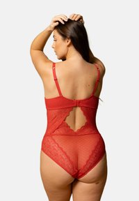 Bodysuit en dentelle rouge avec un dos transparent, présentant un bord festonné et une texture à pois. Des bretelles réglables complètent le design.